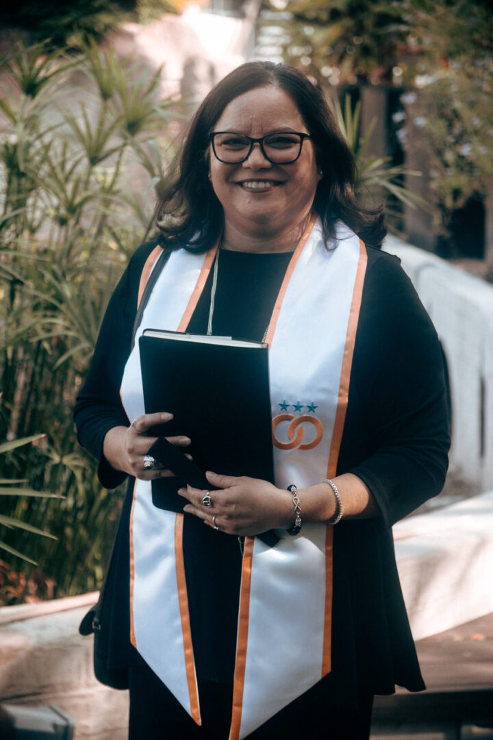 Woman in graduation attire holding folder.